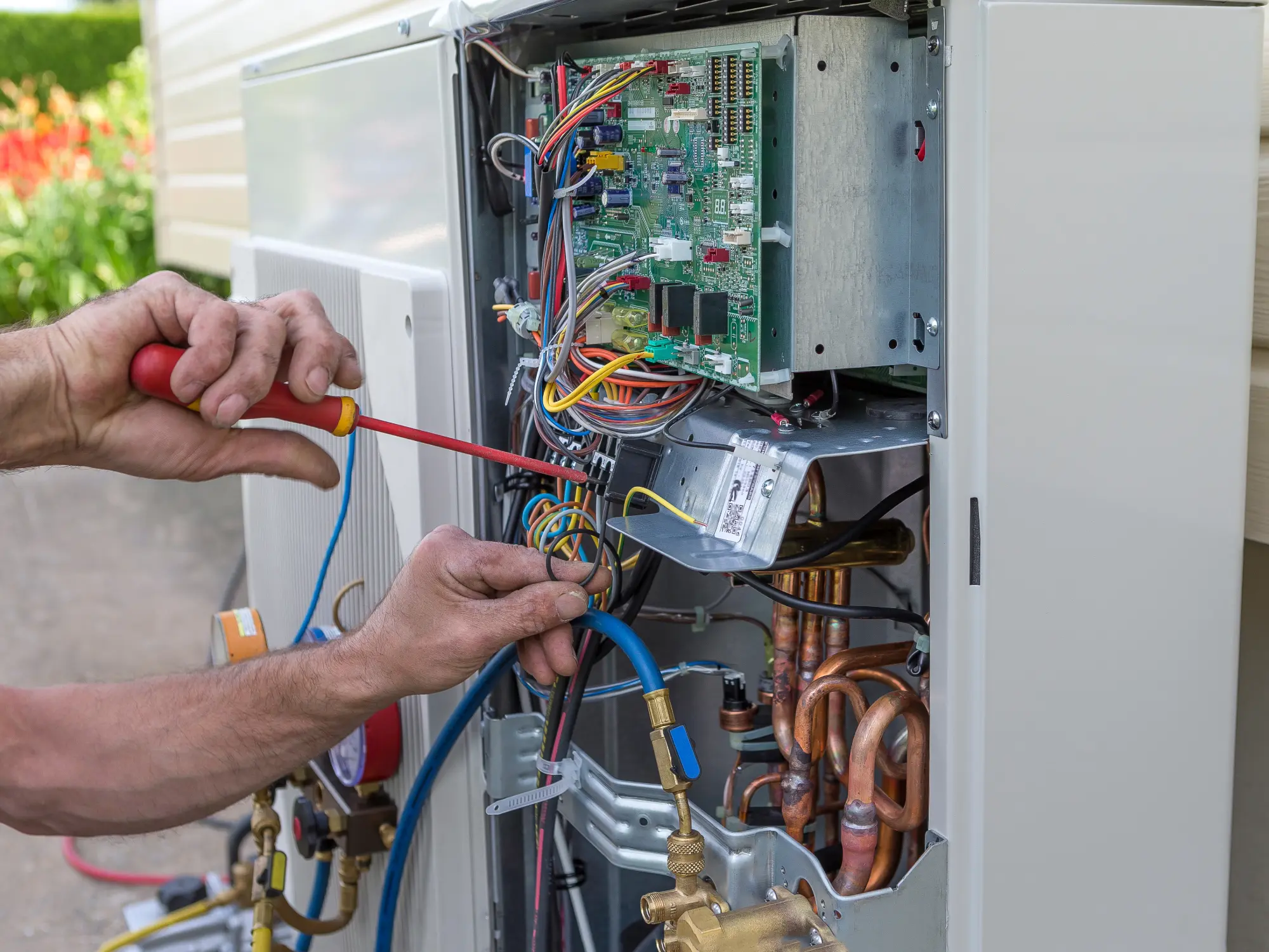 A technician checking the electrical control board and compressor wiring of a heat pump with a screwdriver.