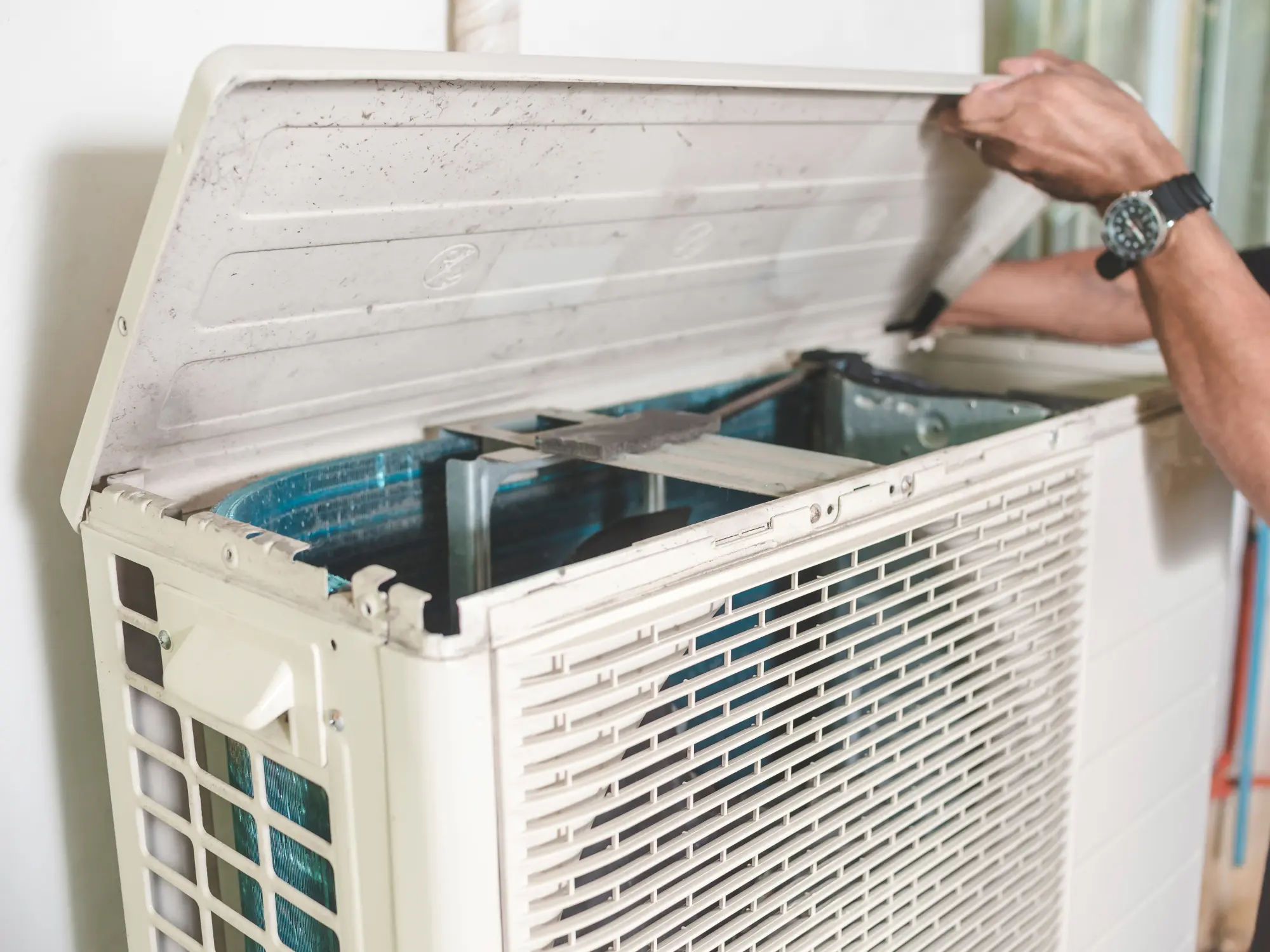 An HVAC technician opening the top cover of an air conditioning unit to inspect for airflow restrictions.