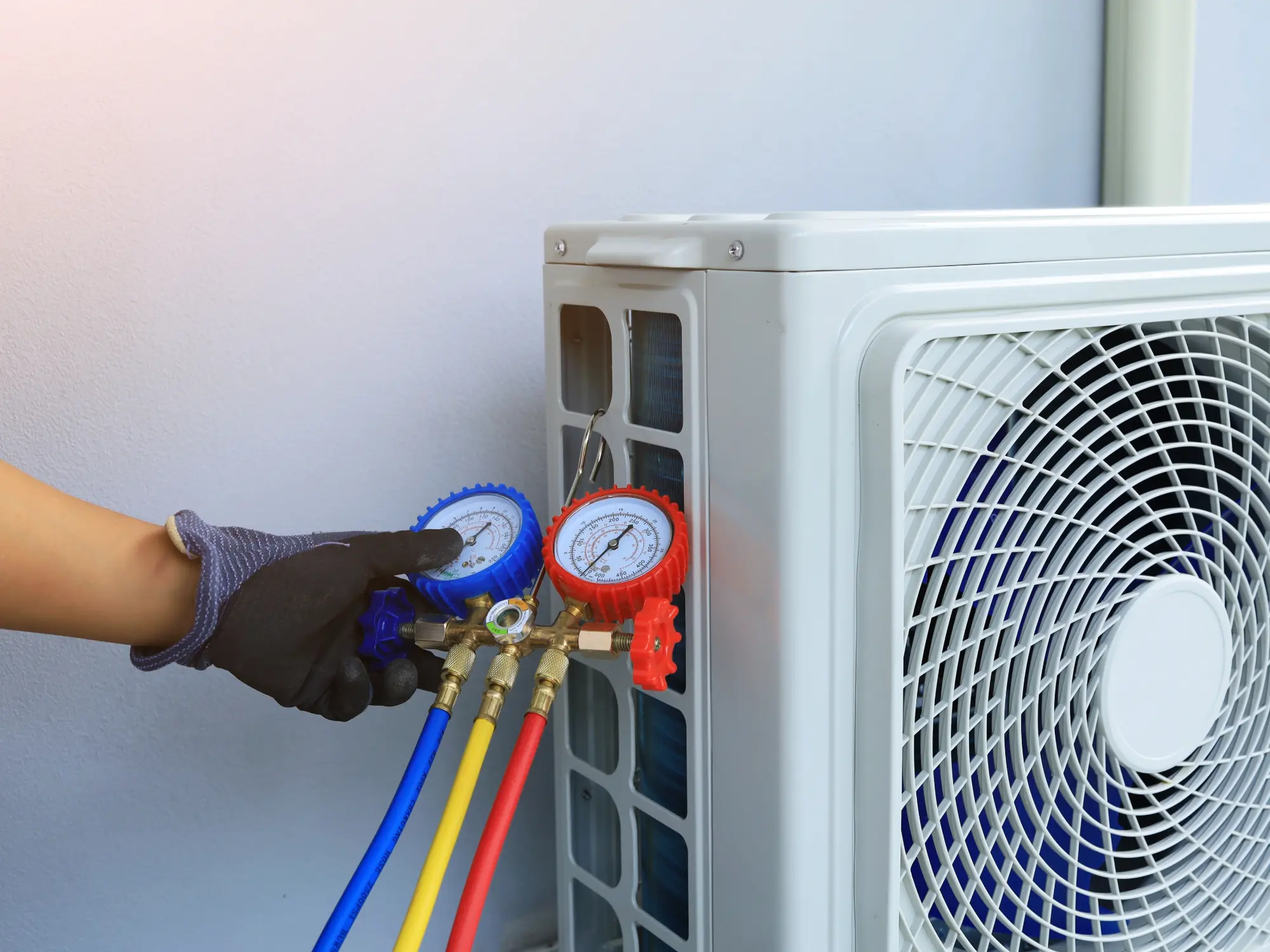A professional technician connecting blue and red pressure gauges to a heat pump to check for a refrigerant leak.